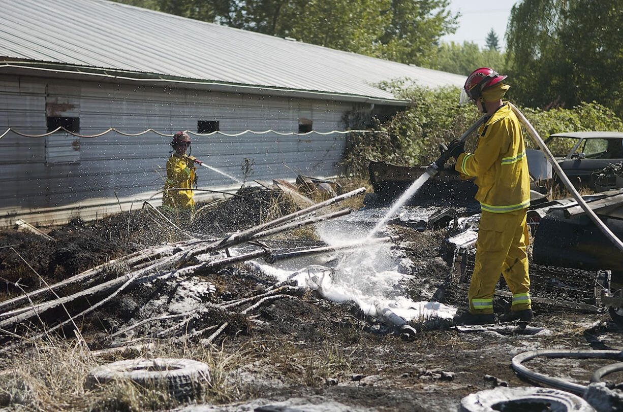 Clark County Fire &amp; Rescue firefighters spray charred ground after a fast moving grass fire sparked between two sheds in Battle Ground Friday afternoon.