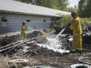 Clark County Fire &amp; Rescue firefighters spray charred ground after a fast moving grass fire sparked between two sheds in Battle Ground Friday afternoon.