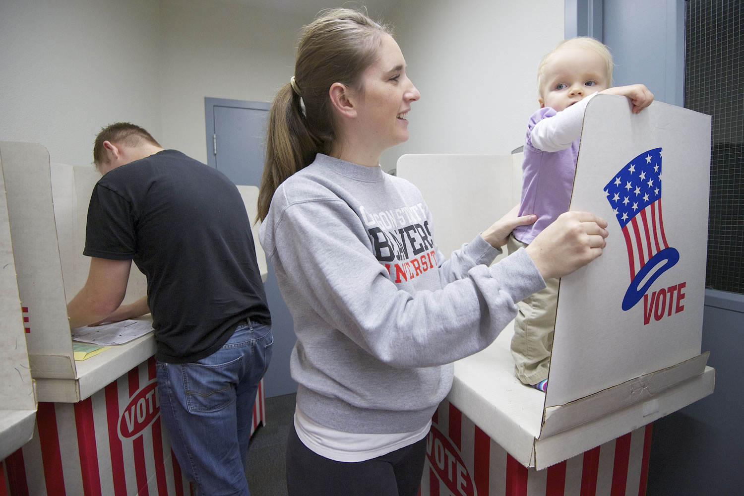 Jake Wannamaker, left, votes Monday at the Clark County Elections Department in Vancouver while his wife Kayla keeps an eye on 1-year-old daughter Alyvia.