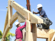 Suspended by heavy cable attached to a reach forklift's beefy hooks, a huge truss is gently lowered into place as a worker from Arrow Timber Framing hammers the tenon into a corresponding mortise in the support beam.