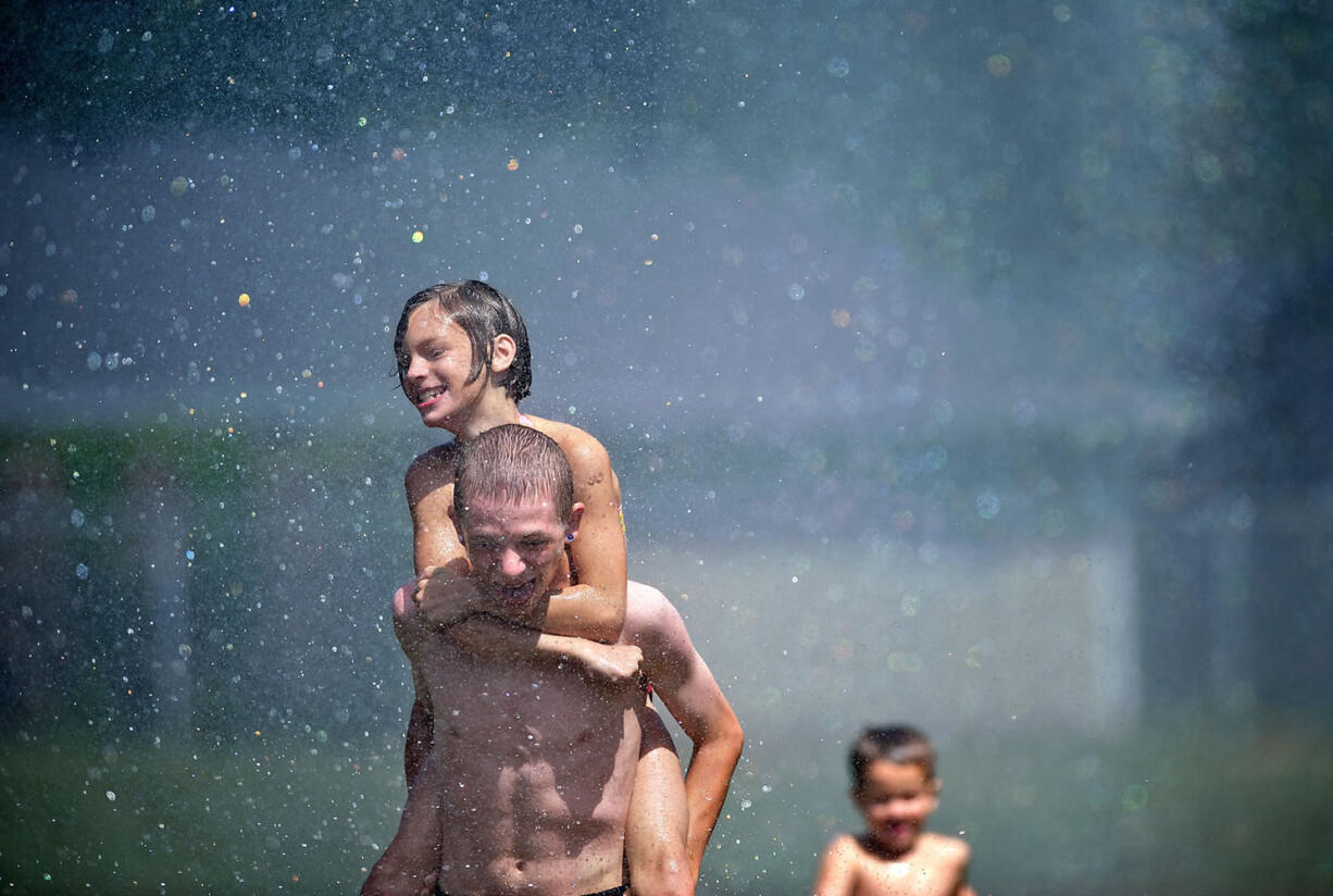 Brooklyn McDonald, 10, gets a ride on the back of Kjorgen Hammer, 17, through a stream of water provided by Camas-Washougal firefighters who opened a fire hydrant at Hamlik Park in Washougal on Thursday to help kids cool off.