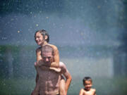 Brooklyn McDonald, 10, gets a ride on the back of Kjorgen Hammer, 17, through a stream of water provided by Camas-Washougal firefighters who opened a fire hydrant at Hamlik Park in Washougal on Thursday to help kids cool off.