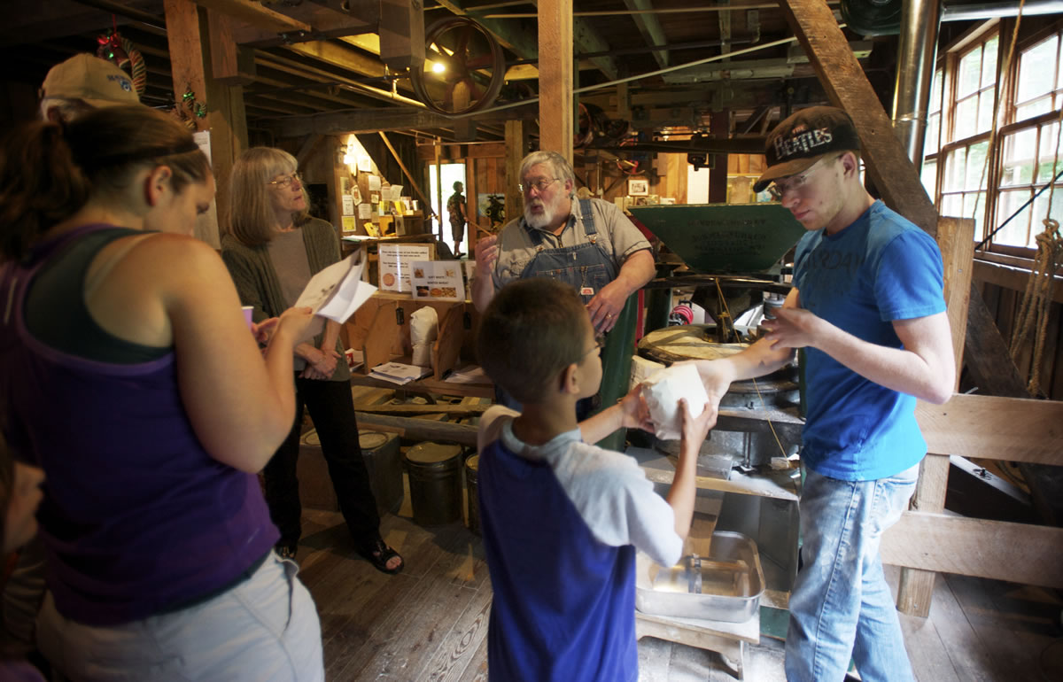 Charles Fallihee, 21, right, is a Clark College baking student who's learning how to operate the 160-year-old milling apparatus behind him.