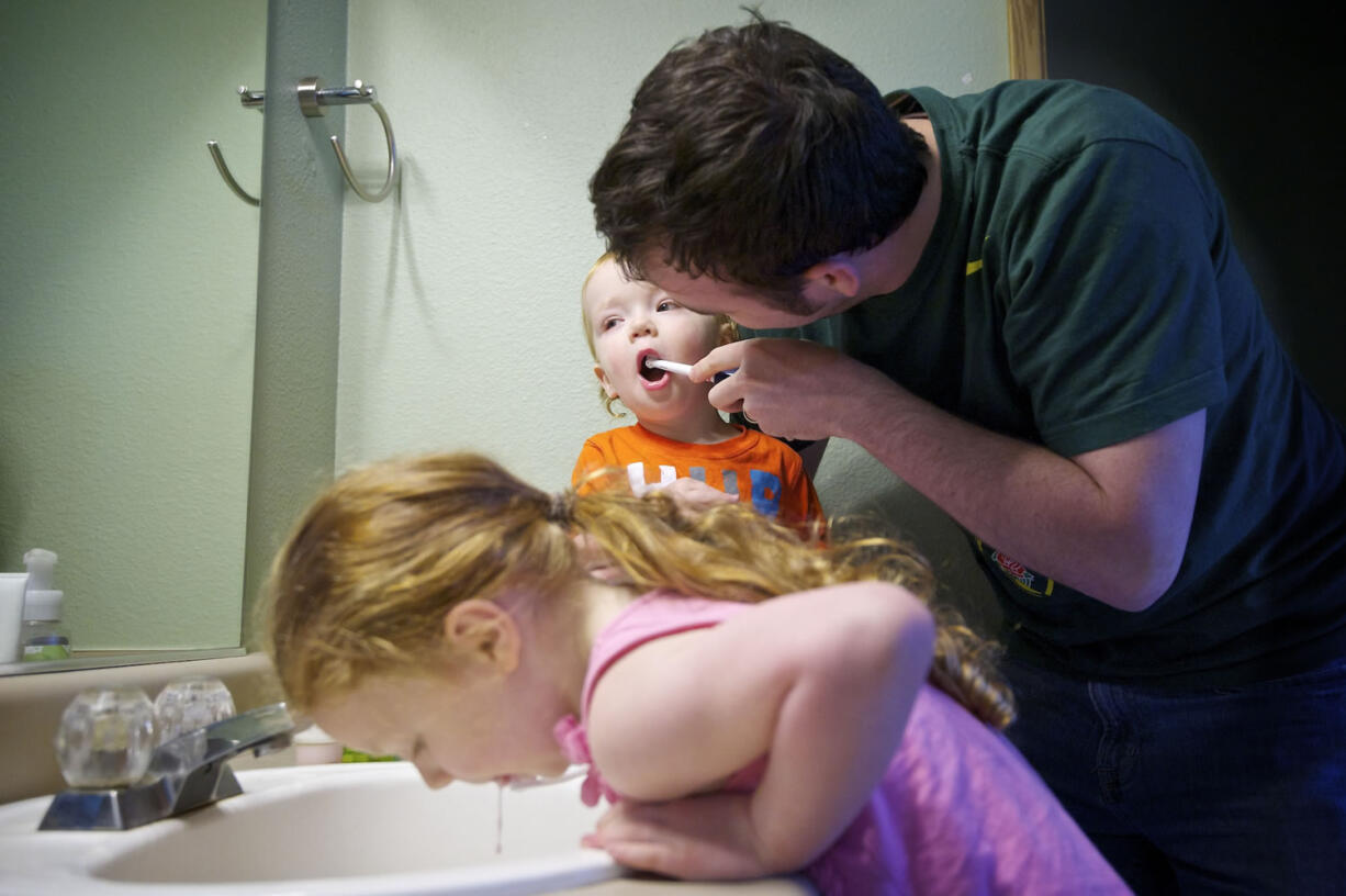 T.J. Green, 34, right, helps Ryland, 1, and Alex, 4, lower left, brush their teeth after breakfast at their Hazel Dell home.