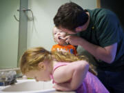 T.J. Green, 34, right, helps Ryland, 1, and Alex, 4, lower left, brush their teeth after breakfast at their Hazel Dell home.