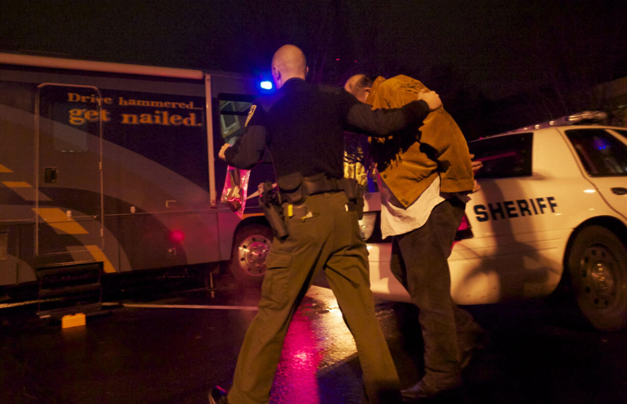 Deputy Chris Luque of the Clark County Sheriff's Office leads a suspected drunken driver into WSP's mobile Impaired Driving Unit during the annual Night of 1,000 Stars DUI crackdown in early December. The name is meant to evoke police badges shining in the night.