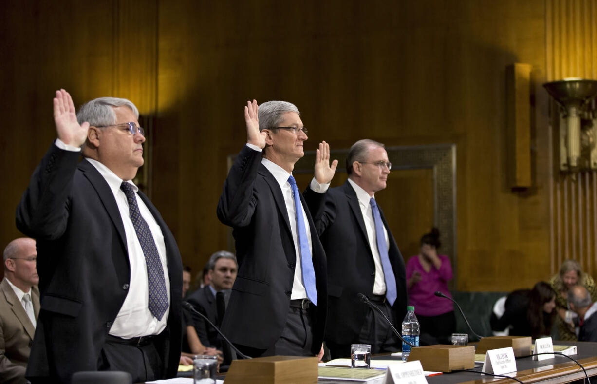 Apple CEO Tim Cook, center, flanked by Peter Oppenheimer, Apple's chief financial officer, left, and Phillip A.