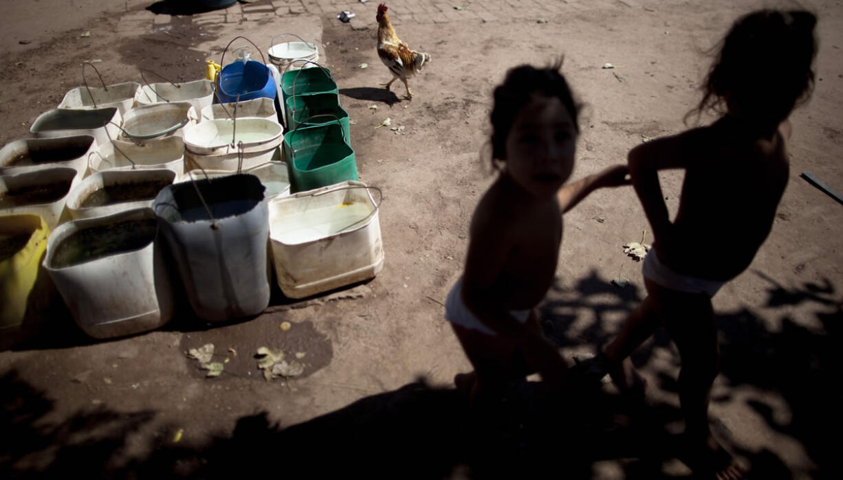 Erika, left, and her twin sister Macarena, who have chronic respiratory illness, play in March in their backyard near recycled agrochemical containers filled with water that is collected to flush their toilet, feed their chickens and wash their clothes, near Avia Terai, Argentina.