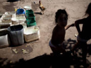 Erika, left, and her twin sister Macarena, who have chronic respiratory illness, play in March in their backyard near recycled agrochemical containers filled with water that is collected to flush their toilet, feed their chickens and wash their clothes, near Avia Terai, Argentina.