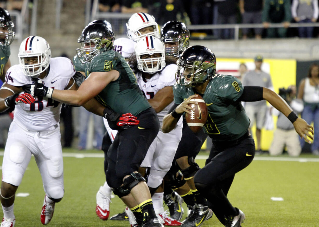 Oregon quarterback Marcus Mariota, right, looks for room to run as Nick Cody (61), a Hockinson High grad, keeps an Arizona defender at bay Saturday night.