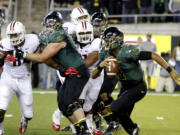 Oregon quarterback Marcus Mariota, right, looks for room to run as Nick Cody (61), a Hockinson High grad, keeps an Arizona defender at bay Saturday night.