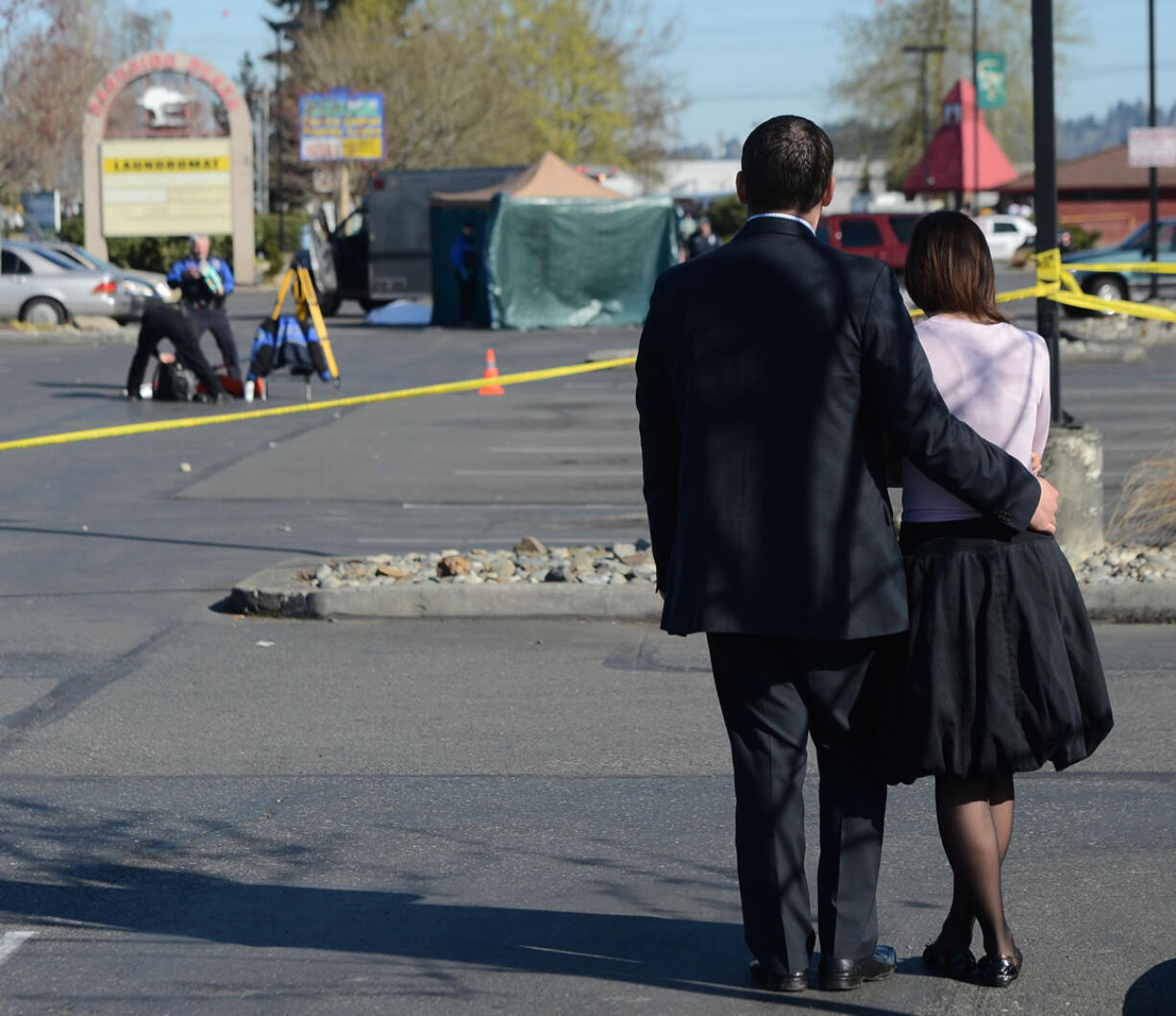 A couple watch Auburn police process the crime scene area where four people were shot and three were killed at the Sports Page in the Parkside Plaza at Auburn on Sunday