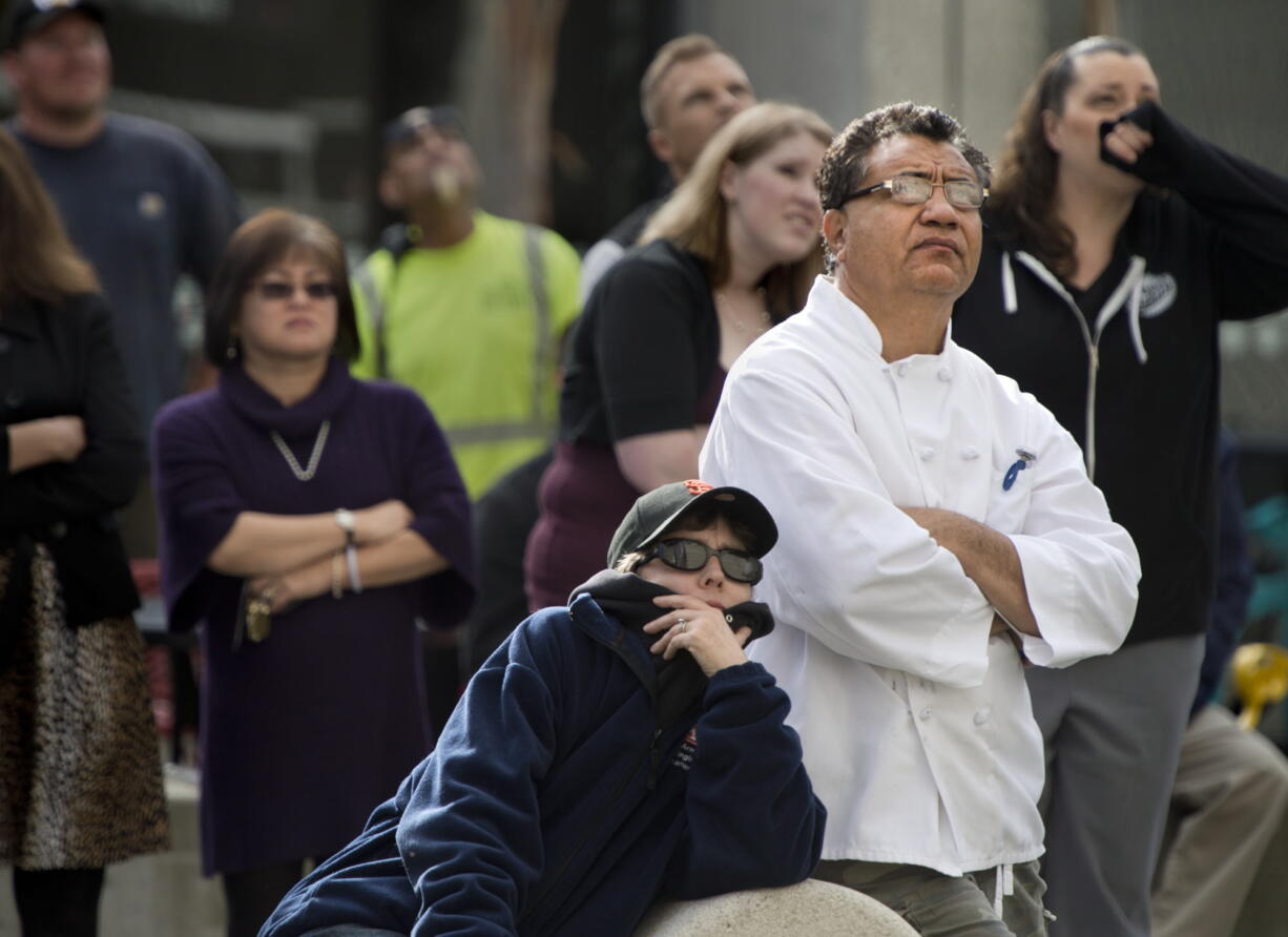 People gather near 13th and J streets to watch firefighters as they recover the body a man hanging from a rope tied to a balcony.