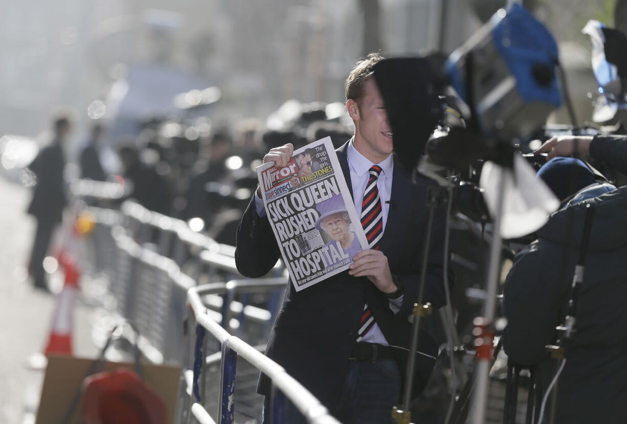 A TV correspondent holds up a British national newspaper showing headlines about Queen Elizabeth II, who was admitted to the King Edward VII hospital in London on Sunday.