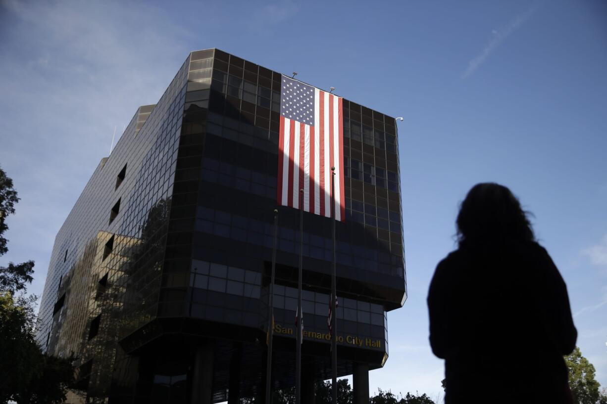 Emily Petrus, a worker for San Bernardino County, pauses to look at a large flag hanging on San Bernardino City Hall on Monday in San Bernardino, Calif. County employee&#039;s returned to work today after Wednesday&#039;s mass shooting. Thousands of employees of San Bernardino County are preparing to return to work Monday, five days after a county restaurant inspector and his wife opened fire on a gathering of his co-workers, killing 14 people and wounding 21.  (AP Photo/Jae C.