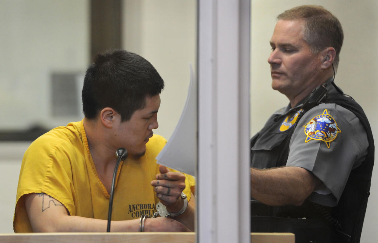 An officer in the Anchorage jail court removes the paperwork that Jerry Andrew Active was using to shield his face during his arraignment on charges of murder and sexual assault of a minor on Sunday in Anchorage, Alaska.