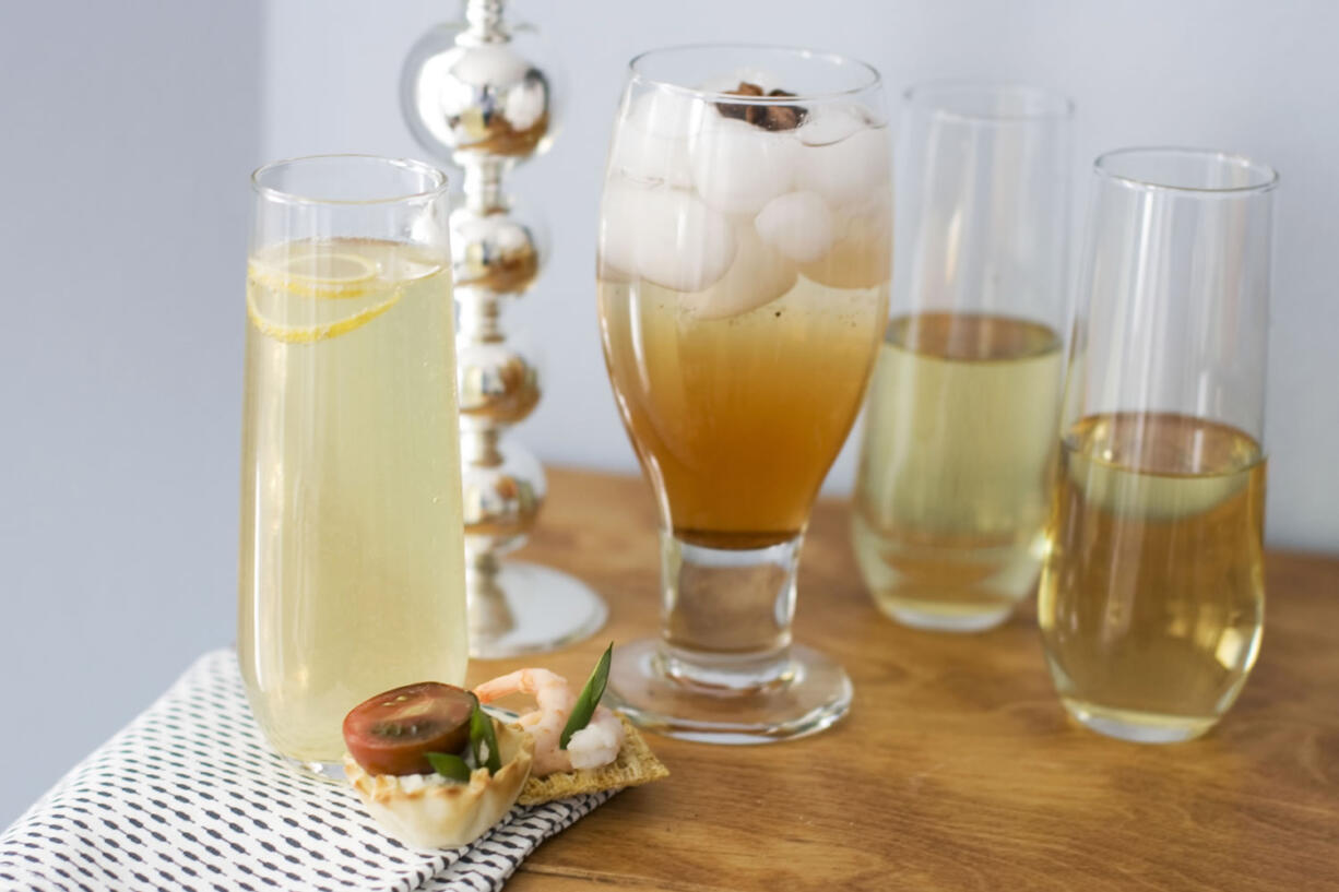 A glass of citrus bubbly with a small curl of lemon on top, from left, a glass of spiced rose-pomegranate spritzer with a star anise on top, and two glasses of sparkling wine, with canapes are shown on a table in Concord, N.H.