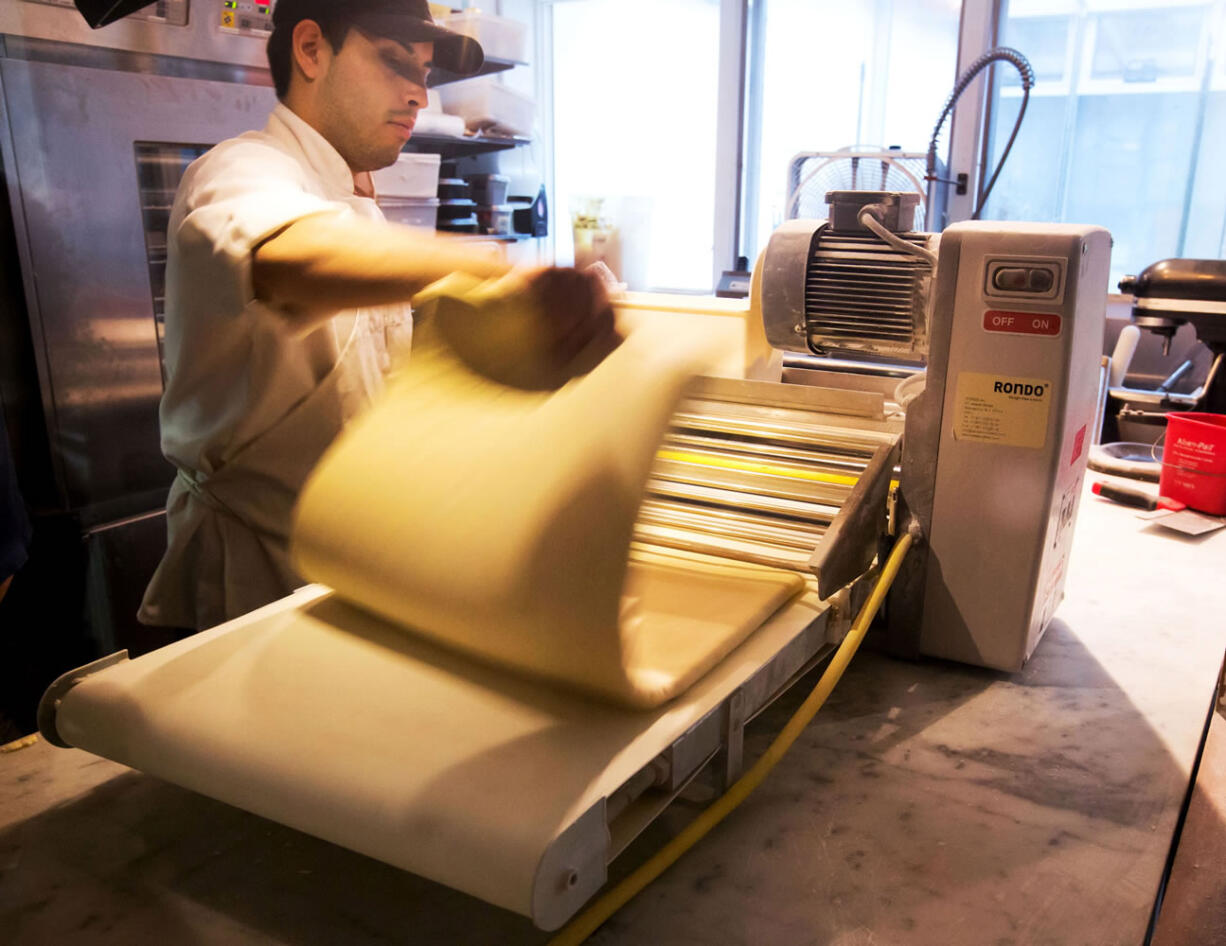 This June 3 photo shows a worker putting dough through a roller to make Cronuts, croissant-donut hybrid, at New York's Dominique Ansel Bakery in New York.