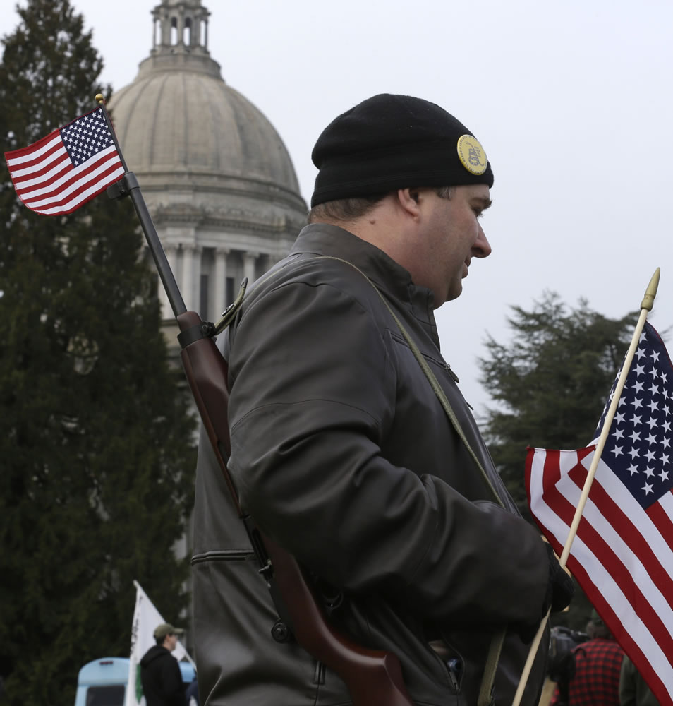 Christopher Knight of Everett displays a U.S. flag in the barrel of his Ruger 10/22 rifle as he attends a gun rights rally Friday at the Capitol in Olympia.