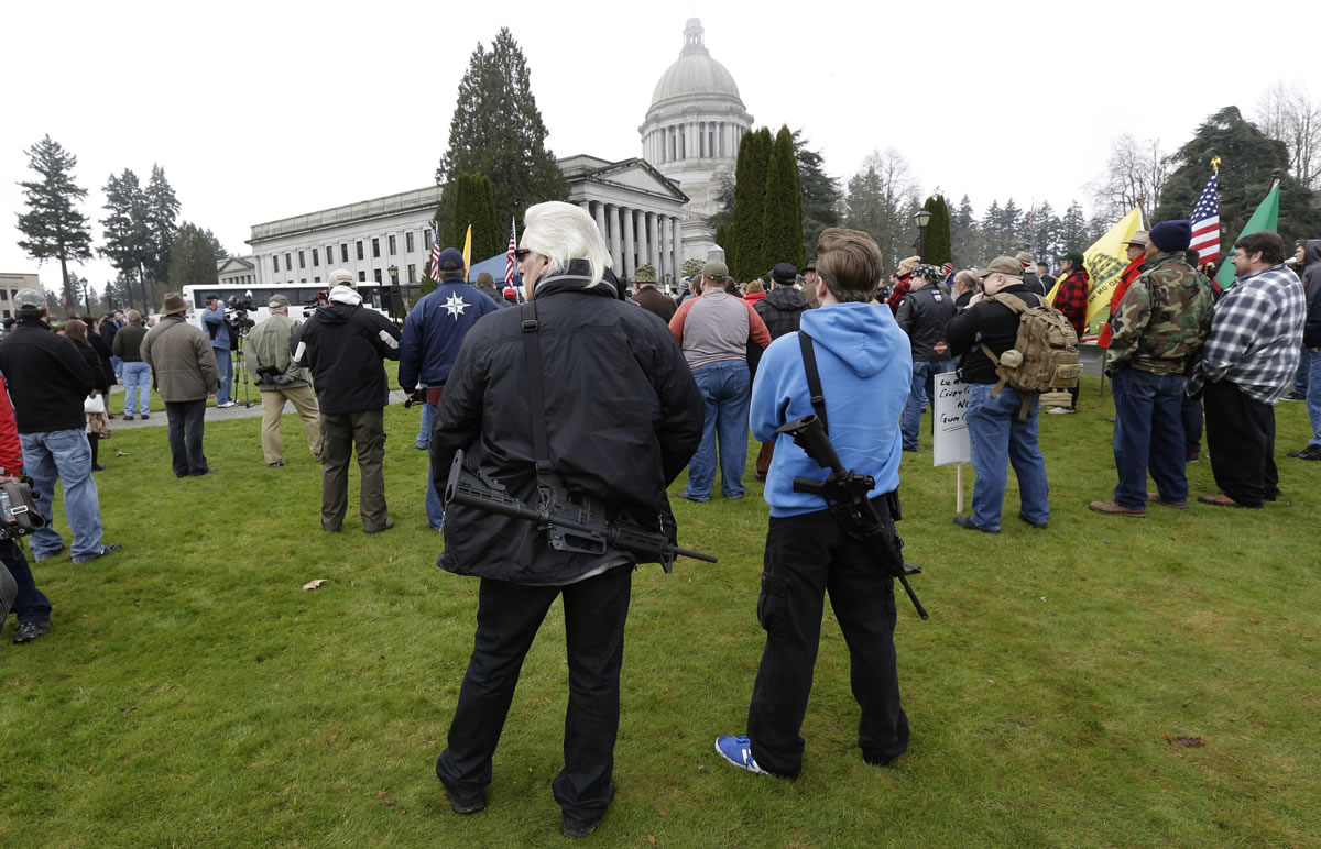 Dan Tidwell, center left, and his son, Thaddeus, center right, both of Gold Bar, wear their AR-15 rifles as they attend a gun rights rally Friday at the Capitol in Olympia.