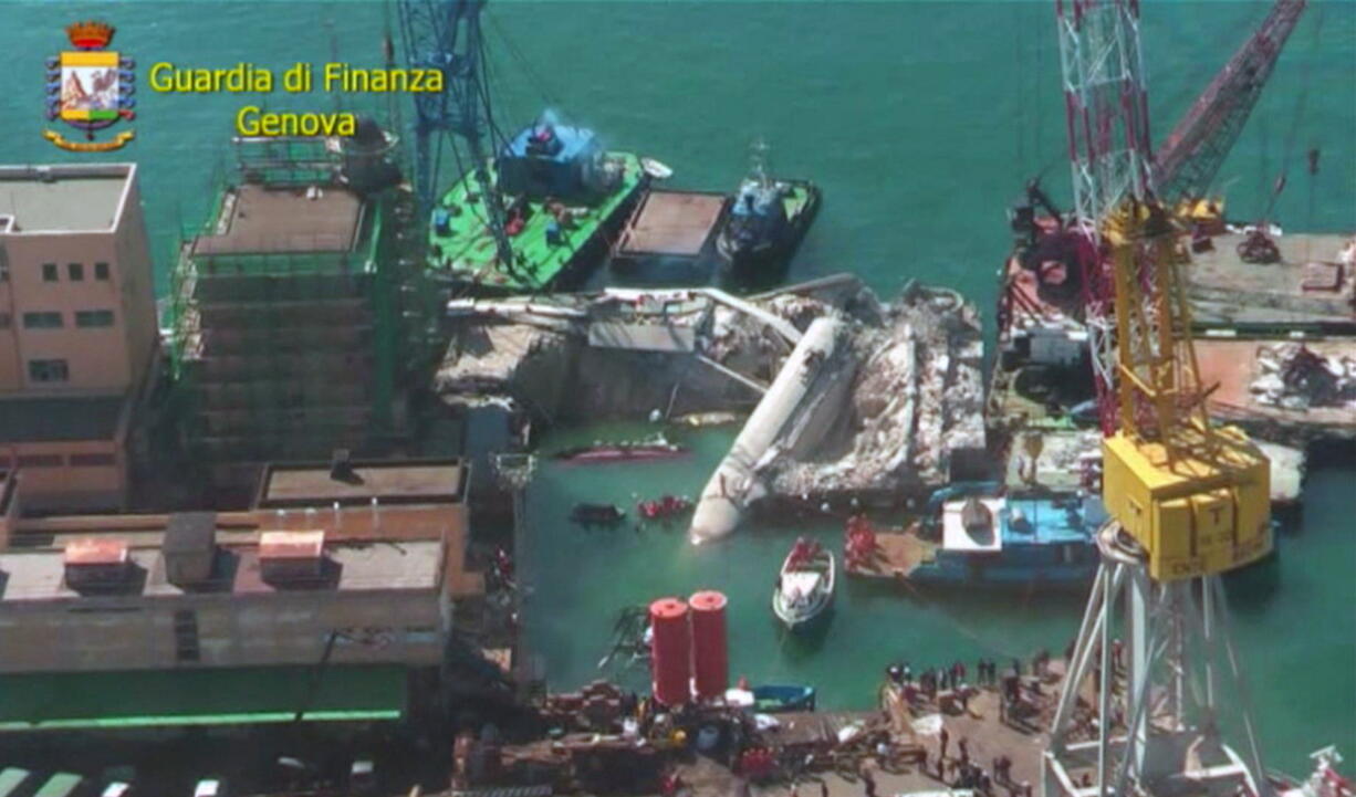 In this image from video, search and rescue operations continue Wednesday at the site where the cargo ship Jolly Nero crashed into the harbor and toppled the port control tower, center, on Tuesday night in Genoa, Italy.