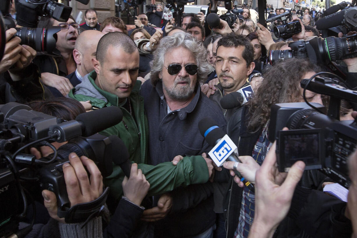 Comic-turned-politician Beppe Grillo, at center with sunglasses, is surrounded by media as he leaves a hotel after a meeting with the elected members of his Movimento 5 Stelle movement in Rome.