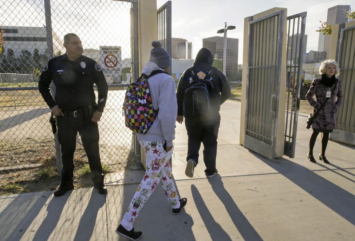 Los Angeles School Police officer Alex Camarillo, far left, and school officials welcome back area students heading back to school at the Edward R. Roybal Learning Center in Los Angeles Wednesday, Dec. 16, 2015. Students are heading back to class a day after an emailed threat triggered a shutdown of the vast Los Angeles Unified School District. The shutdown abruptly closed more than 900 public schools and 187 charter schools across Los Angeles.