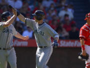 Seattle Mariners' Justin Smoak, center, is congratulated by teammate Kyle Seager after hitting a two-run home run as Los Angeles Angels catcher Hank Conger looks on during the sixth inning Sunday.