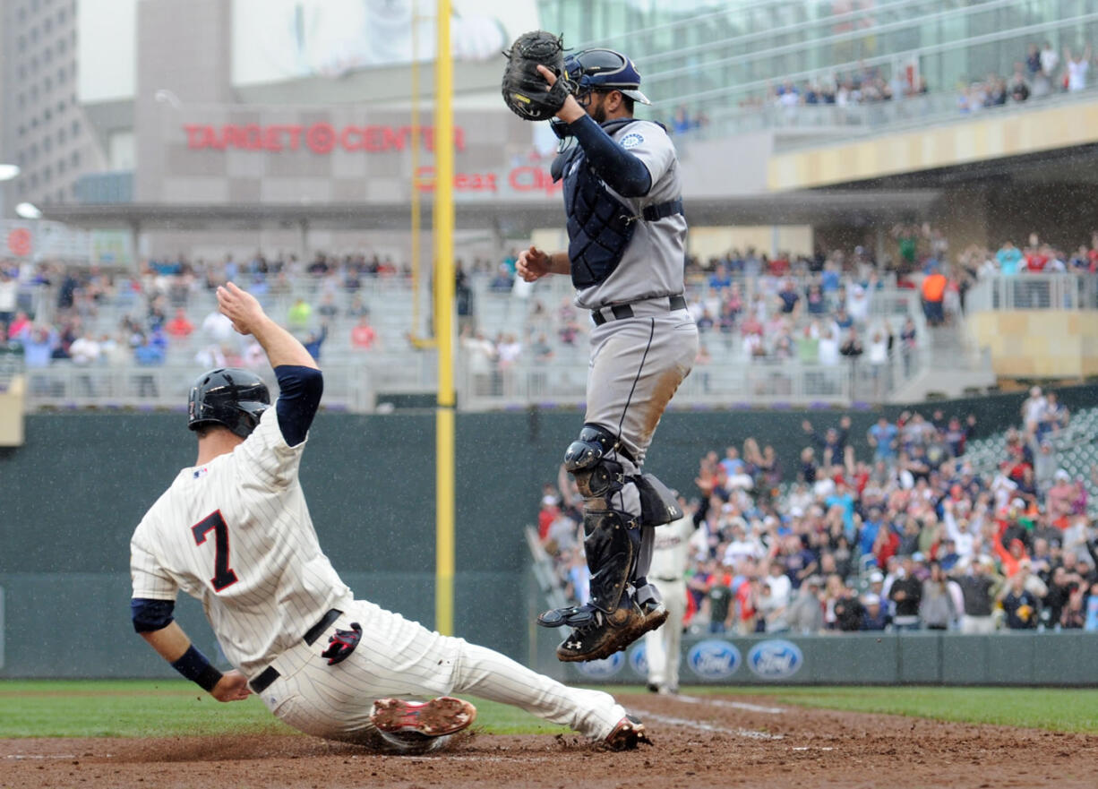 Joe Mauer (7) scores the game-winning run as  Mariners catcher Kelly Shoppach jumps to reach the throw.