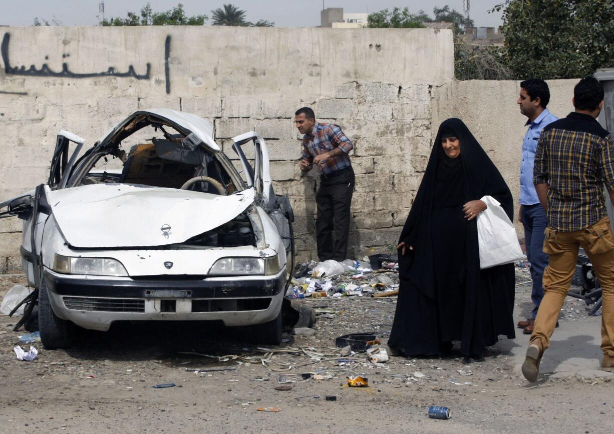 People inspect a damaged car at the scene of a car bomb attack in Zayona neighborhood of eastern Baghdad, Iraq, Wednesday, March 20, 2013. Iraqi officials say a car bomb in eastern Baghdad has killed and wounded a few people on the 10th anniversary of the US-led invasion, the day after a series of well-coordinated attacks left scores dead.