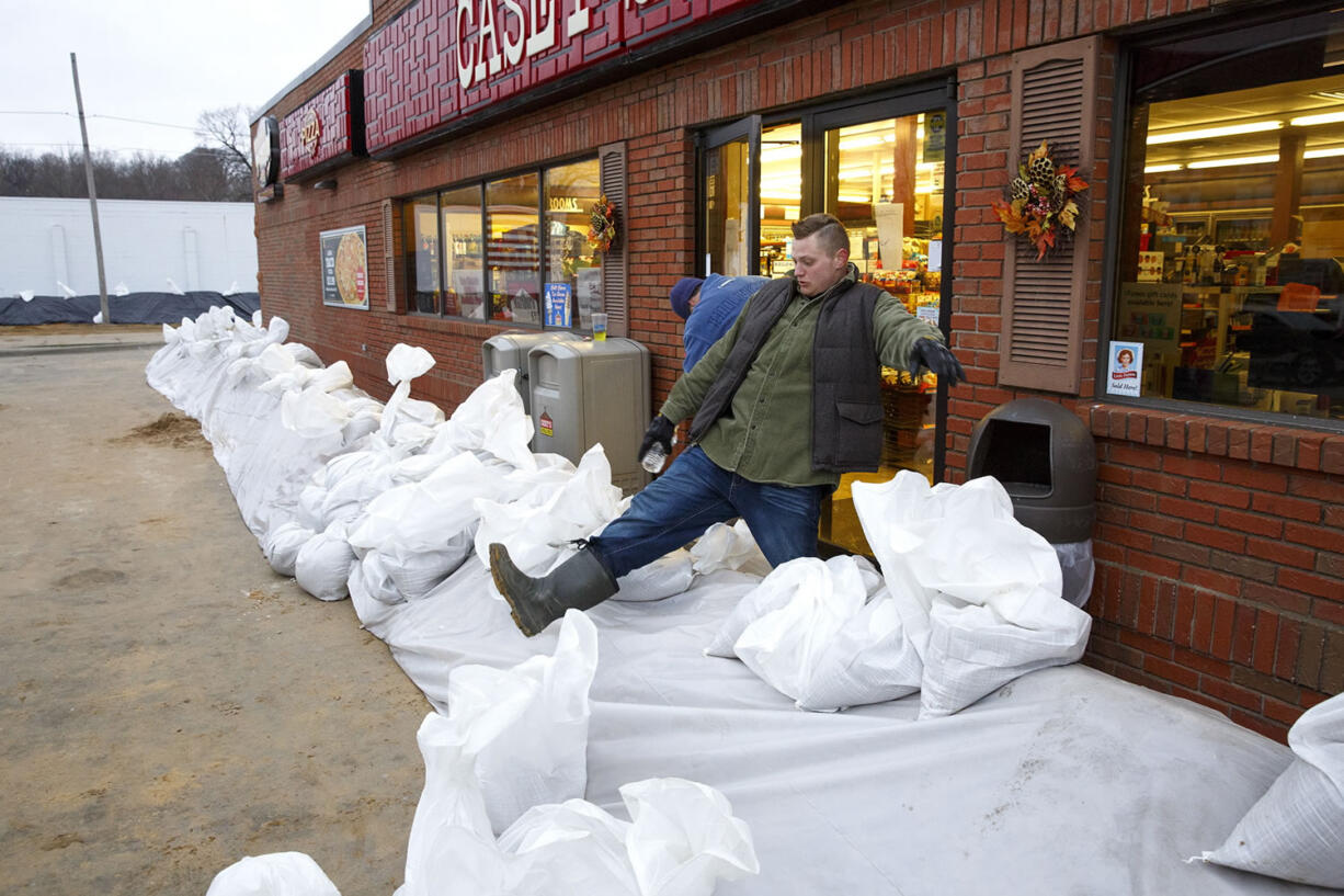 David Fritch, associate manager of the Casey&#039;s in Petersburg, Ill., climbs over a sand berm built to hold off approaching water from the Sangamon River on Wednesday. Fritch and store manager Clayton A. Roberts closed and locked up the store, like many of the other businesses near the river. Volunteers were building a five-block-long emergency levee in an effort to save more than 150 houses and several businesses from damage.