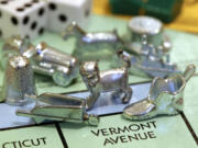 The newest Monopoly token, a cat, center, rests on a Boardwalk deed next to other tokens still in use including the wheelbarrow, left, and the shoe, right.