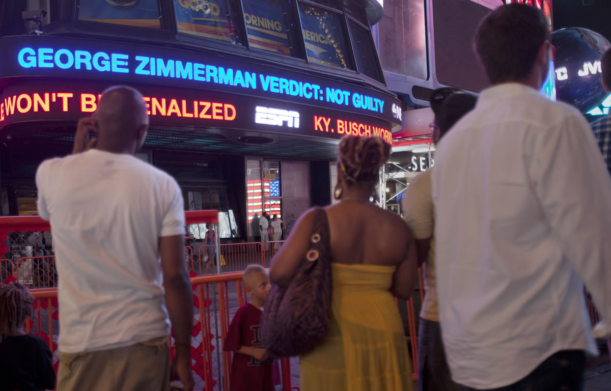 People watch a news ticker in Times Square deliver the news that George Zimmerman was found not guilty.