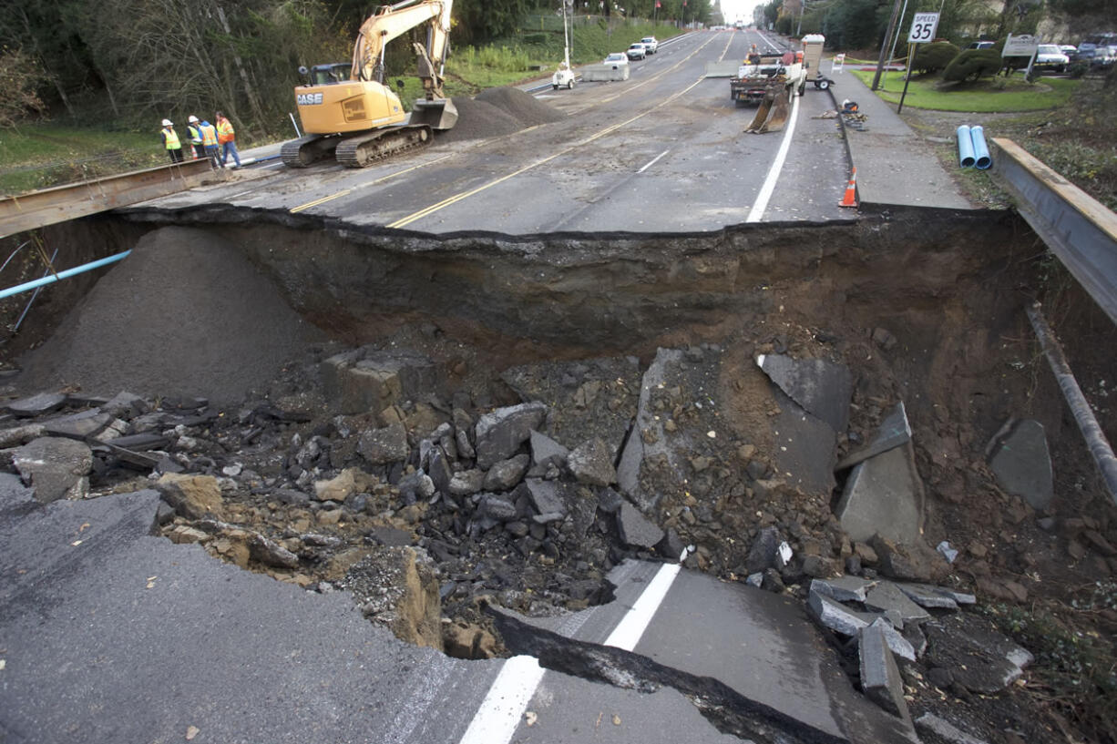 Maintenance personnel look at a large sinkhole on Kane Drive in Gresham, Ore., on Wednesday. Torrential rains pummeled parts of the Pacific Northwest early Wednesday, causing mudslides and flooding roads.