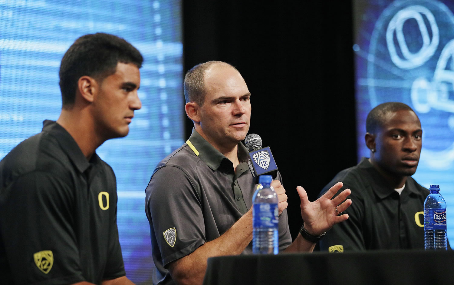 Oregon coach Mark Helfrich, center, talks to reporters as he is flanked by quarterback Marcus Mariota, left, and cornerback Ifo Ekpre-Olomu during the Pac-12 football media day, Friday.