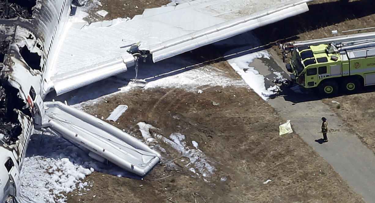 A firefighter stands by a tarpaulin sheet covering a body near the wreckage of the Asiana Flight 214 airplane after it crashed at the San Francisco International Airport in San Francisco on July 6.