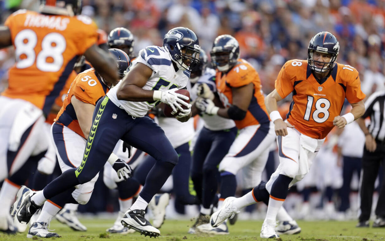 Denver quarterback Peyton Manning (18) looks on as Seattle's K.J. Wright, center, runs back an interception in the first half Saturday.