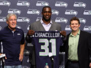 Seattle Seahawks head coach Pete Carroll, left, and general manager John Schneider, far right, pose for photos after announcing a four-year extension to the contract of safety Kam Chancellor, middle, during an NFL football news conference on Monday, April 22, 2013, in Renton, Wash.