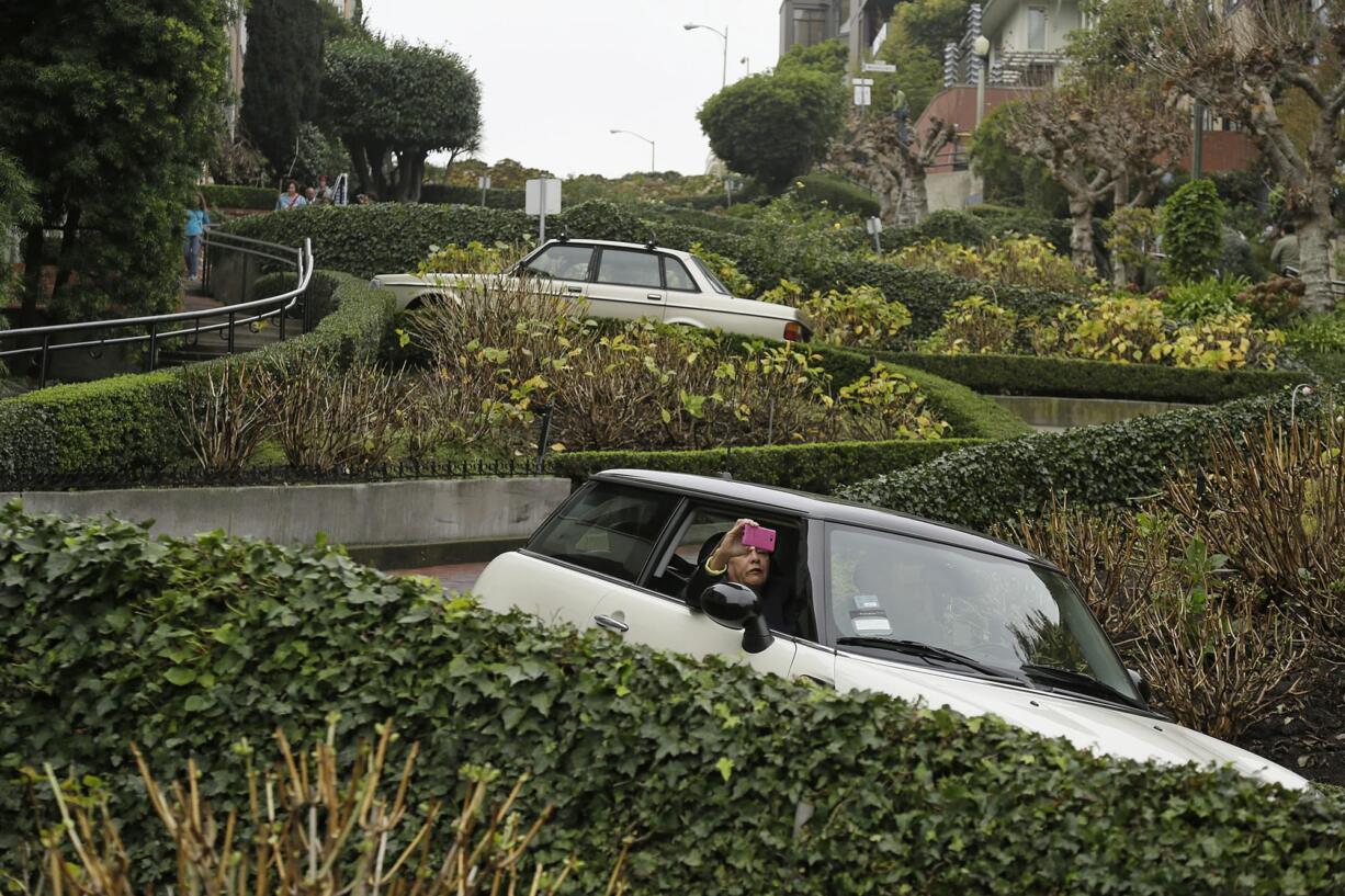 A woman takes a selfie while riding down the crooked section of Lombard Street in San Francisco. The section of eight hairpin turns, one-way, downhill, starts at Hyde Street.