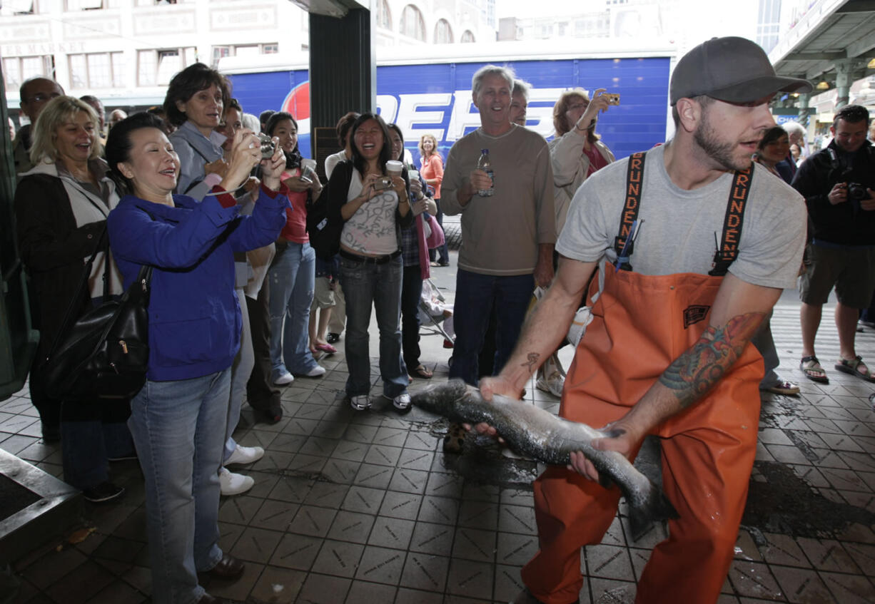 Justin Hall throws a salmon to a co-worker behind the counter at Pike Place Fish at Pike Place Market in Seattle.