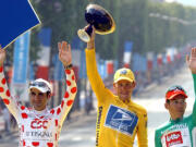 Lance Armstrong, center, waving from the podium as he holds the winner's trophy July 28, 2002, along with best sprinter Robbie McEwen, of Australia, right, and best climber Laurent Jalabert, of France, after the 20th and final stage of the Tour de France cycling race between Melun and Paris.