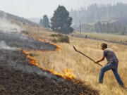 Homeowner David Firth tries to beat back a brush fire heading toward his home as a wildfire burns Tuesday in Cle Elum.