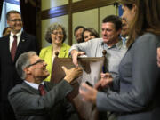 Gov. Jay Inslee, seated left, turns to shake hands with Alan Northrop, a former Clark County resident, after Inslee signed into law a measure that would allow people who have been wrongfully convicted to seek state compensation for the years they were imprisoned on Wednesday in Olympia.