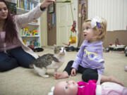 Simone Tipton, left, dangles a cat toy as she and daughter Scarlette, 2, play with their new kitten, Doc. Tipton and husband Matt searched for six months to find an amputee cat for their daughter, who had an arm amputated during a battle with cancer.