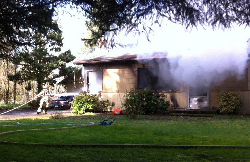 Firefighter Kelby Kiedrowski of East County Fire &amp; Rescue works to knock down a Sunday afternoon fire at 23702 N.E. 54th Street in Vancouver.