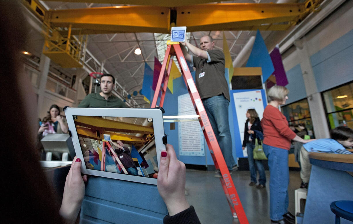 Washington State University Vancouver student Madi Kozacek, foreground left, points an iPad at an object representing the digital hot spots that will be installed on a display automobile at the Oregon Museum of Science and Industry in Portland. OMSI's Jeff Varner, center, holds the object at the appropriate height. At right is WSUV student Jason Clark.