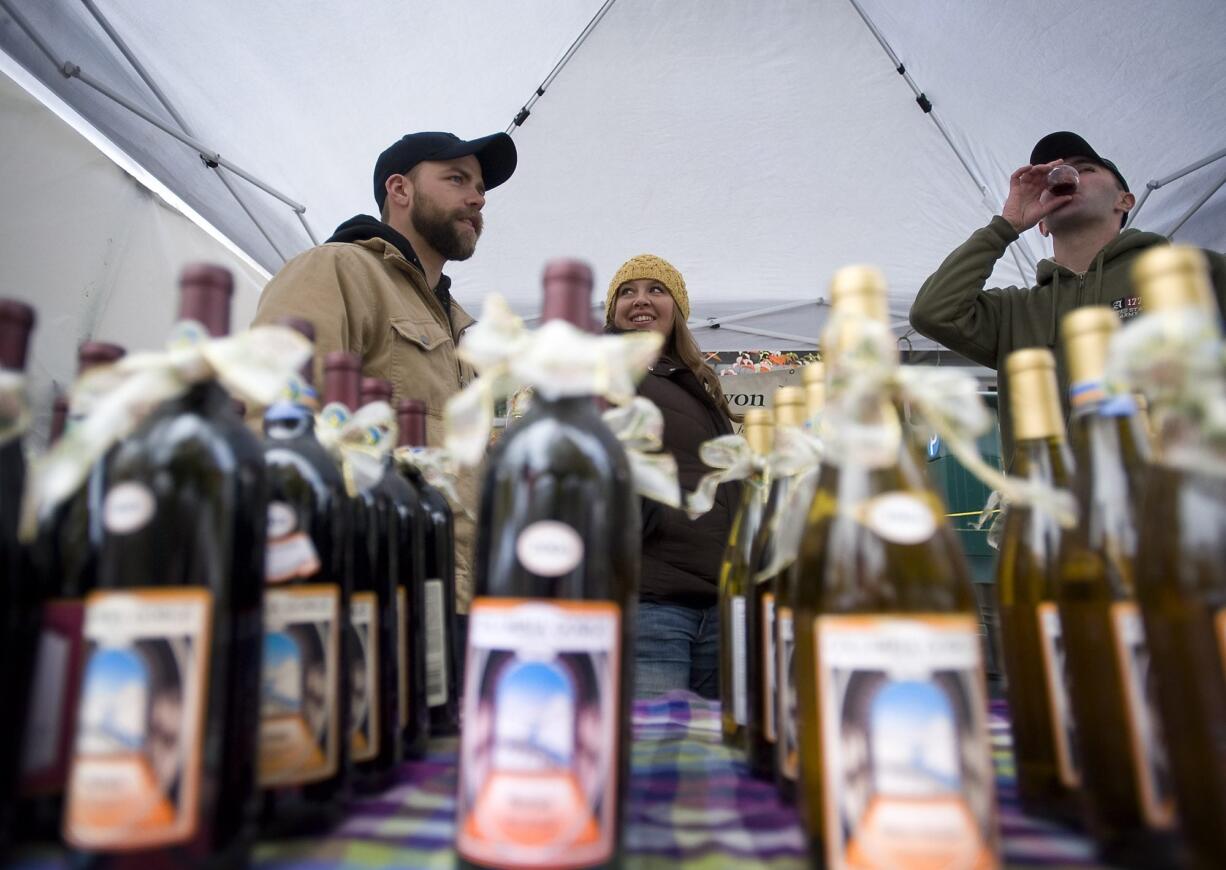 Gordie Blair, left, 27, of Vancouver, and his wife Danielle Blair, 27, work the Klickitat Canyon Winery booth at the Vancouver Farmers Market, as Tim Doherty samples their Lemberger on Nov.