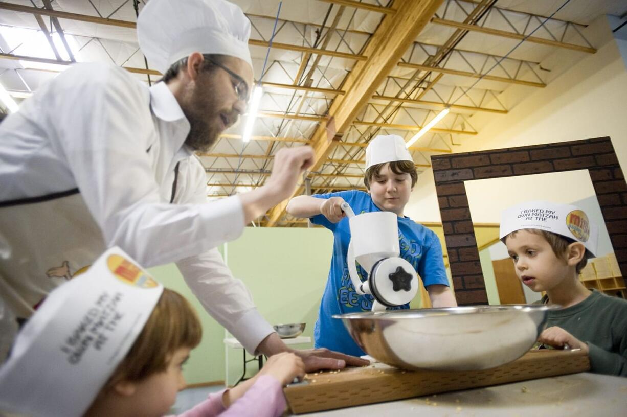 Rabbi Shmulik Greenberg shows Shalom Dinberg, 3, Cameron Hatton, 12, and Levi Greenberg, 5, how to grind wheat to make matzo at the Gan-Garrett Jewish preschool.