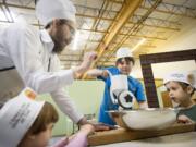 Rabbi Shmulik Greenberg shows Shalom Dinberg, 3, Cameron Hatton, 12, and Levi Greenberg, 5, how to grind wheat to make matzo at the Gan-Garrett Jewish preschool.