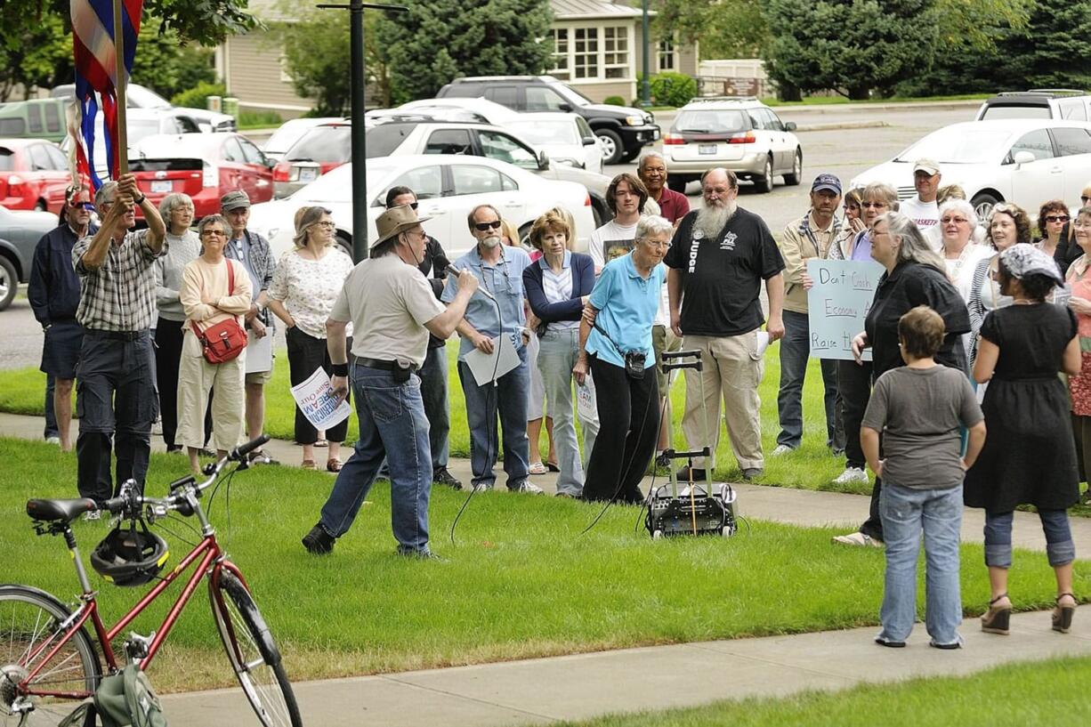 Tom Scharf, left, in hat, speaks to protesters gathered outside U.S. Representative Jaime Herrera Beutler's congressional office Tuesday to voice their opposition to the representative's views on the U.S.